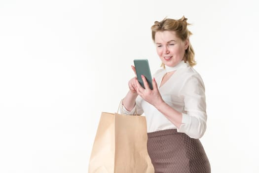 Cheerful woman shopping, holding smartphone looking at screen and reading online messages and browsing offers with sales and discounts. Female in white blouse and brown skirt. Studio shot on white
