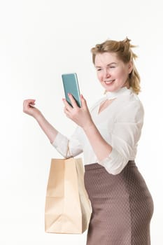 Middle aged adult woman holding shopping bags with purchases, smiling while looking at phone, using app on smartphone. Caucasian ethnicity 49 years old woman shopper. Studio shot on white background