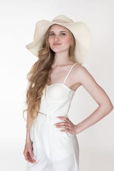 Portrait of European fashion model wearing her new clothes, to dress up straw hat, white sculpting cupped corset top and trousers. Headshot young female with blonde long wavy hair on white background