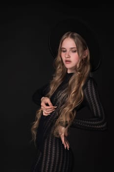 Portrait of blonde woman looking down, exudes beauty and glamour as she poses on black background. Fashion model with long blonde hair, wearing black short tight knitted dress, wide-brimmed felt hat