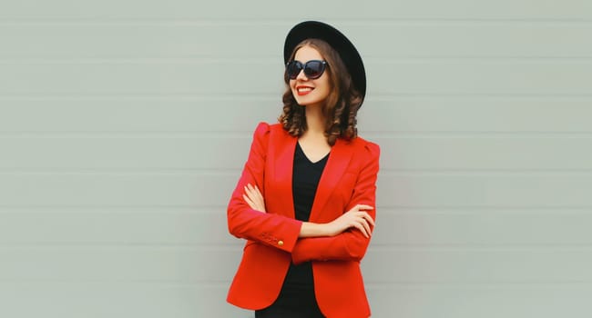 Stylish elegant woman crossed arms posing in business suit, red blazer jacket, black round hat