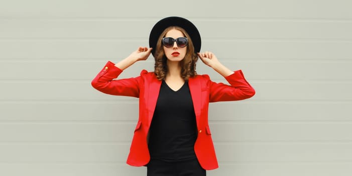 Stylish elegant woman posing in business suit, red blazer jacket and black round hat