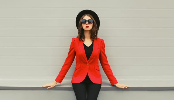 Stylish elegant woman posing in business suit, red blazer jacket and black round hat