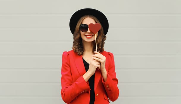 Beautiful happy woman with sweet red heart shaped lollipop on stick in black round hat