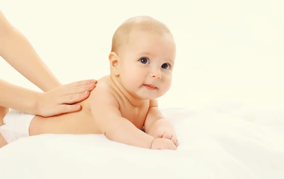 Close up mother gives massage to baby lying on the bed on white background, child and health concept