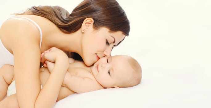 Portrait of happy young mother kissing cute baby lying on the bed together at home