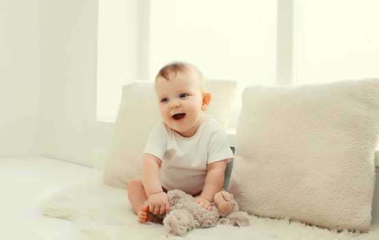 Happy cute little baby playing with teddy bear toy on the floor in white room at home