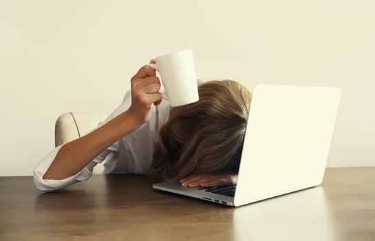 Tired overworked sleepy woman employee holding cup asking to drink extra coffee working with laptop sitting at desk in office in morning