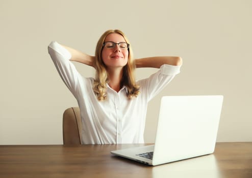 Relaxed happy young woman take a break meditates working with laptop sitting at desk in office or home