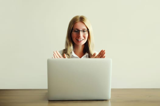 Happy young woman working on laptop greets communicates with friends via video call sitting at desk in office or home