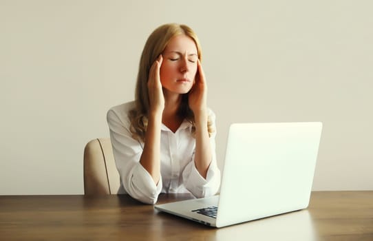 Tired overworked woman employee suffering from headache, migraine, working with laptop sitting at desk in office in morning