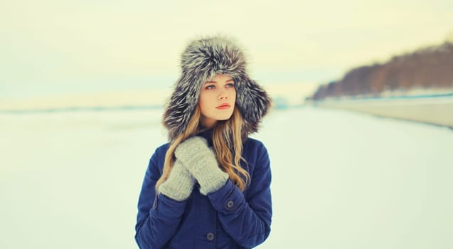 Portrait of beautiful blonde young woman posing in winter hat outdoors in park