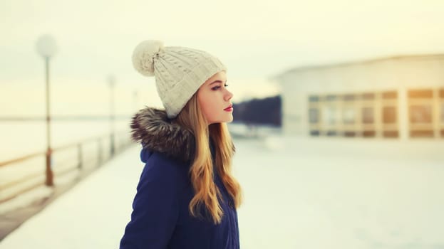 Portrait of beautiful blonde young woman posing in winter hat outdoors in park