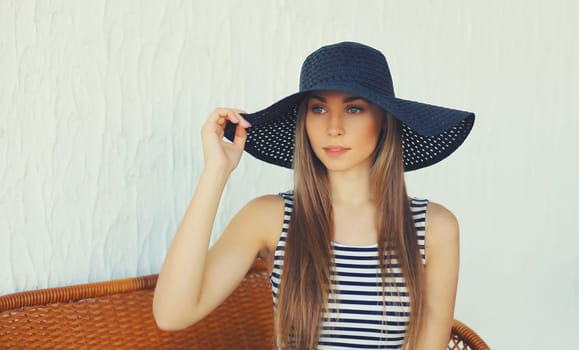 Portrait of beautiful blonde young woman in summer straw hat resting on the chair