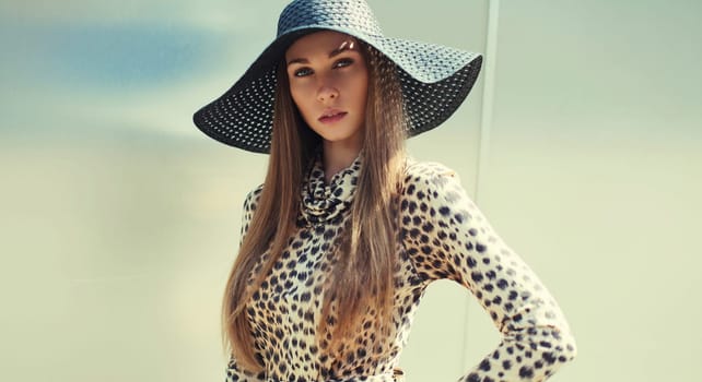 Portrait of beautiful blonde young woman wearing summer straw hat, leopard dress in the city