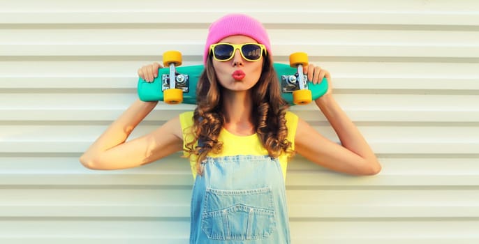 Summer portrait of happy cheerful young woman posing with skateboard in colorful clothes on white background