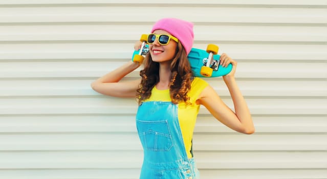 Summer portrait of happy cheerful smiling young woman with skateboard in colorful clothes on white background