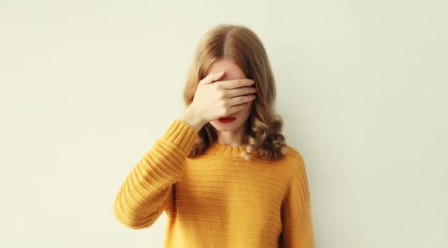 Upset sad young woman keeps hand palm on face, regrets or sorrow gesture on head on studio background