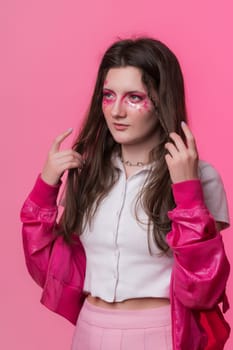 Portrait of young adult woman with pink stage make-up with sequins and arrows painted on face, dressed in pink jacket, skirt and white t-shirt. Studio shot of informal female on colored background