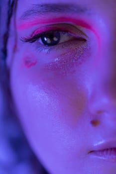 Half young female face with shiny stage make-up with sparkles and arrows illuminated with blue and pink neon light. Studio shot of Caucasian ethnicity adult woman looking away. Part of photo series