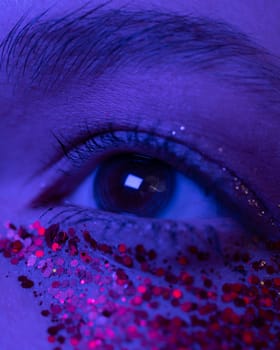 Extreme close-up view of female eye with shiny make-up with sparkles. Cinematic macro shot of female eye illuminated pink-blue color neon light. Selective focus, part of photo series