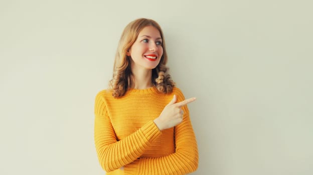 Portrait of happy smiling young woman pointing her finger to the side and looking away on studio background, blank copy space for advertising text