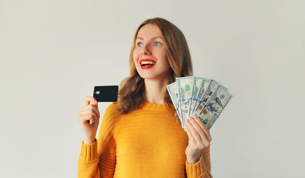 Portrait of happy smiling young woman holding plastic credit bank card and cash money in dollar bills