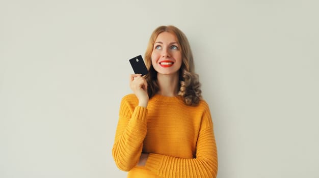 Portrait of happy smiling young woman holding plastic credit bank card and looking up on studio background