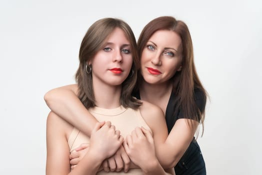 Portrait of happy mom and teenage daughter. 43-year-old mother stands behind and gently hugging her daughter. Happiness and togetherness concept. Studio shot, part of photo series