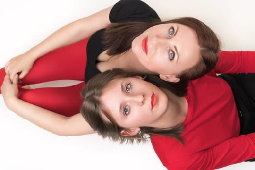 Top view of mom and daughter sitting with their backs to each other and put their heads on each other's shoulders. Both women looking up at camera. Studio shot, part of photo series