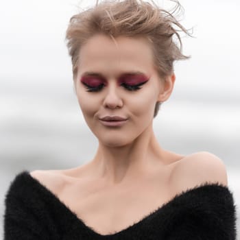Portrait of blonde woman with short hair and bright makeup posing outdoors, with eyes closed, in front of white natural background. Soft selective focus adds lovely touch to stunning woman's portrait