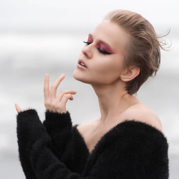 Portrait of blonde woman with her eyes closed. Fashion model with bright makeup and short hair posing outdoors against white natural background. Soft selective focus makes portrait even more beautiful