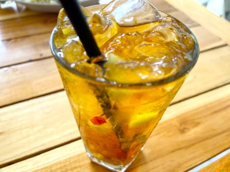 fresh mix fruit cocktail alcohol drink with rum and whiskey in a clear glass and chunk of ice on a wooden table background