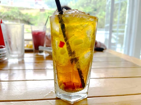 fresh mix fruit cocktail alcohol drink with rum and whiskey in a clear glass and chunk of ice on a wooden table background