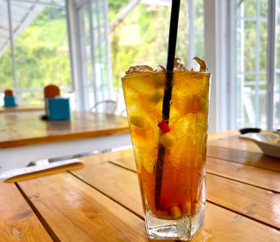 fresh mix fruit cocktail alcohol drink with rum and whiskey in a clear glass and chunk of ice on a wooden table background