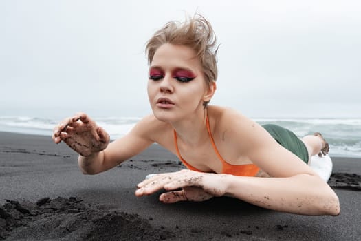 Portrait of woman with bright makeup and closed eyes lying on surfboard on sandy beach, she looks like she in complete harmony with waves. Sports fashion model surfer is epitome of sexuality and grace