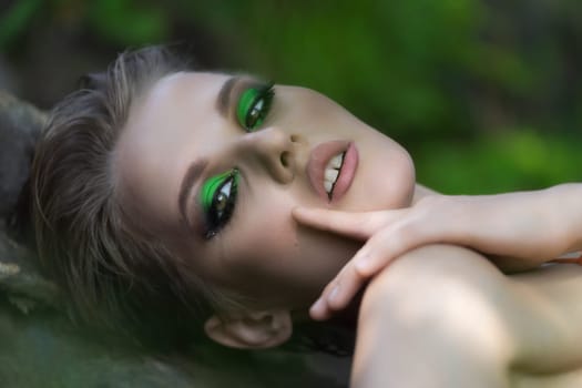 Closeup portrait of authenticity woman with short hair and bright make-up looking at camera. Sexual blonde model relaxation in summer forest, enjoyment outdoors. Selective focus