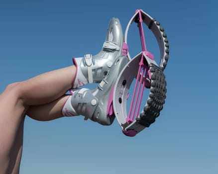 KAMCHATKA, RUSSIA - JUNE 15, 2022: Cropped close-up view of female crossed legs up in air shod in sports Kangoo Jumps boots during outdoor fitness workout on background of blue sky on sunny summer day
