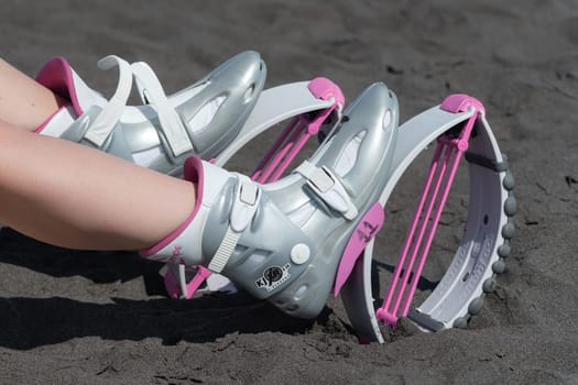 KAMCHATKA, RUSSIA - JUNE 15, 2022: Closeup view of female legs in sports Kangoo Jumps boots on black sandy beach before outdoor aerobic exercising, fitness workout. High angle shot