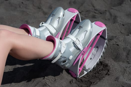 KAMCHATKA, RUSSIA - JUNE 15, 2022: High angle shot female legs in sports Kangoo Jumps shoes on black sandy beach before outdoor aerobic exercising, fitness workout. Closeup trendy jumping boots
