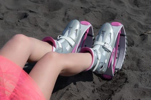 KAMCHATKA, RUSSIA - JUNE 15, 2022: Point of view shot of female legs in sports Kangoo Jumps boots on black sandy beach before outdoor aerobic exercising, fitness workout. Close-up trendy jumping boots
