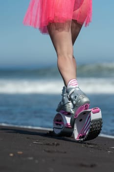 KAMCHATKA, RUSSIA - JUNE 15, 2022: Rear view of female athlete legs in sports Kangoo Jumps boots, running on sandy beach during summer outdoors fitness workout on ocean shore. Low section, crop view