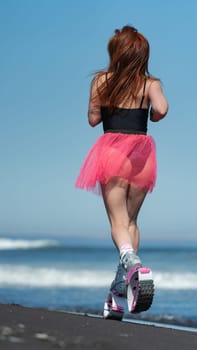 KAMCHATKA, RUSSIA - JUNE 15, 2022: Rear view of sportswoman in sports Kangoo Jumps boots, one piece swimsuit and short skirt running and jumping on black sandy beach during aerobic session workout