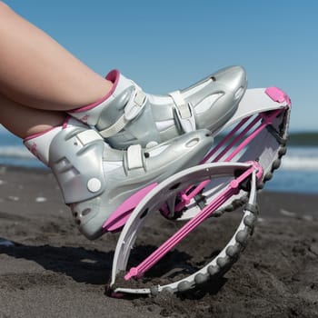 KAMCHATKA, RUSSIA - JUNE 15, 2022: Close-up slim female legs in trendy Kangoo Jumps boots on black sandy beach while resting during aerobic fitness training session workout. Side view, square format