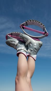 KAMCHATKA, RUSSIA - JUNE 15, 2022: Cropped closeup view of female crossed legs up in air shod in pink Kangoo Jumps boots during fitness exercising outdoors on background blue sky on sunny summer day
