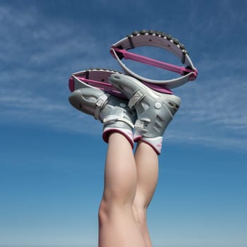 KAMCHATKA, RUSSIA - JUNE 15, 2022: Close-up view of woman crossed legs up in air shod in sports Kangoo Jumps boots during aerobic exercising outdoors on background of blue sky on sunny summer day