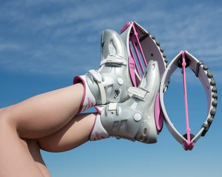 KAMCHATKA, RUSSIA - JUNE 15, 2022: Female crossed legs up in air shod in pink Kangoo Jumps boots during fitness exercising outdoors on background of blue sky on sunny summer day. Cropped closeup view