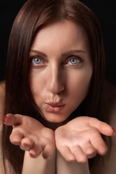 Adult woman blowing lips send air kiss over palms to her boyfriend and looking at camera. Pretty 40-year-old woman with gray eyes demonstrates good feelings. Front view, studio shot black background.