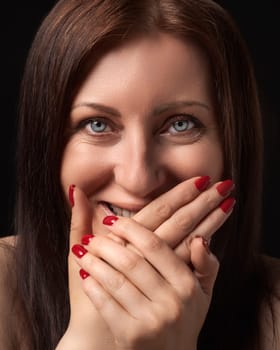 Cheerful charming woman laughing while covering mouth with her hands with red manicure on nails and gazing at camera. Studio portrait of Caucasian ethnicity 40-year-old brunette woman with gray eyes.