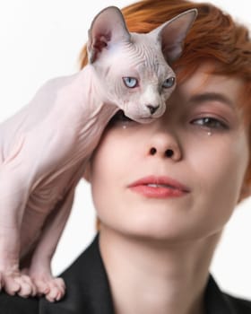 Playful Sphynx Cat standing on shoulder of redhead woman and gently pressed against her face. Studio shot on white background. Selective focus on domestic animal, shallow depth of field. Part series.
